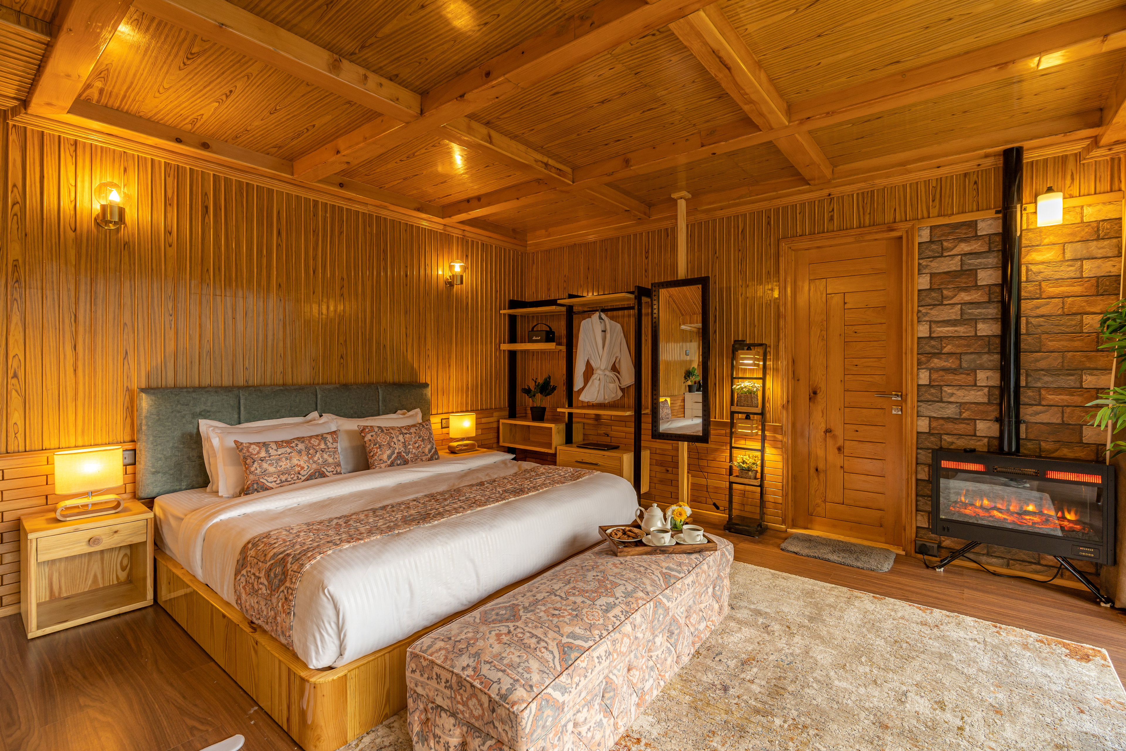 Deodar-panelled bedroom glowing warm, with an electric fireplace set in a brick chimney