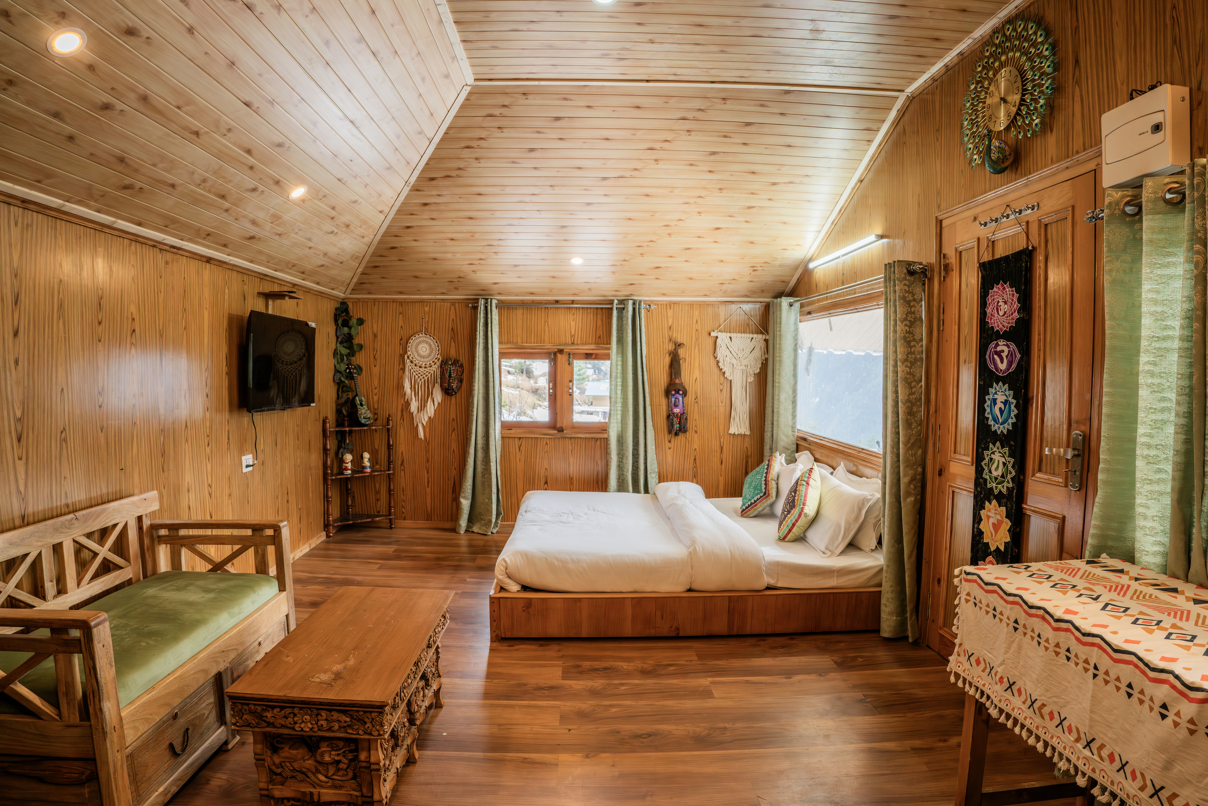 A spacious pine-panelled room with a low wooden bed, television, bench seat and mountain windows